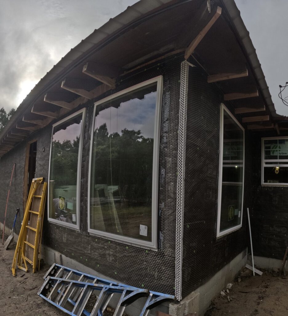 In-progress photo: the exterior wrapped in house wrap with new windows set and foam board along the base