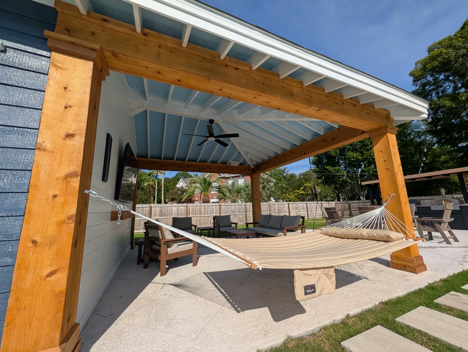 Cedar posts and beams under a haint-blue ceiling, a shiplap wall with a mounted TV, and a hammock
